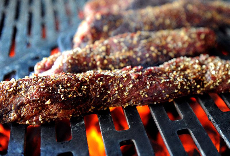 Hanger steak grilling over a charcoal fire on the Hybrid Fire Grill